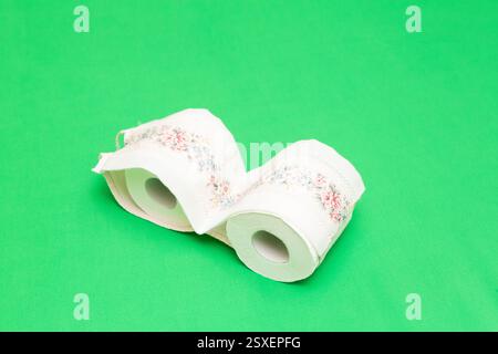 Zwei weiße Toilettenpapierrollen mit rosafarbenen und blauen Blumendekorationen auf einem leuchtend grünen Hintergrund Stockfoto