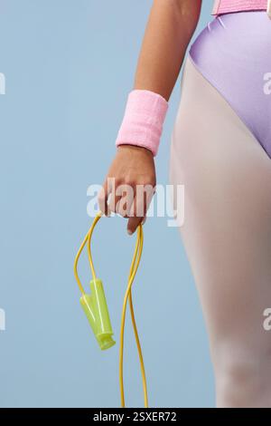 Nahaufnahme von Personen, die mit der Hand ein Sprungseil halten, während sie rosa Armbänder tragen, in sportlicher Kleidung vor pastellfarbenem Hintergrund gekleidet Stockfoto