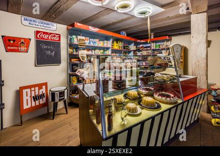 Rekonstruierter Eckladen in Deutschland. In einem deutschen Vintage-Supermarkt werden zum Verkauf stehende Artikel, darunter Kuchen, Süßigkeiten und Haushaltswaren, sowie eine Waage und ein Schild für Barbara Kainer gezeigt. Persil Reinigungsmittel kostet 59 Pfennig. Sattlertorstraße, Forchheim, Bayern, Deutschland Stockfoto