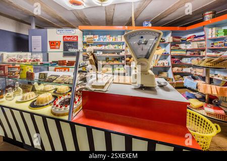 Rekonstruierter Eckladen in Deutschland. In einem deutschen Vintage-Supermarkt werden zum Verkauf stehende Artikel, darunter Kuchen, Süßigkeiten und Haushaltswaren, sowie eine Waage und ein Schild für Barbara Kainer gezeigt. Sattlertorstraße, Forchheim, Bayern, Deutschland Stockfoto