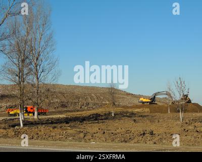 Baumaschinen, die auf einem Erdhügel arbeiten, einen Bagger und einen Planierraupen beim Planieren einer Baustelle oder beim Füllen einer Grube Stockfoto