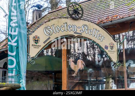 Ein gebogenes Schild mit der Aufschrift „Glocken-Keller“ und dem Wappen der Brauerei Rittmayer spannt sich über den Eingang zu einem Bierkeller im Kellerwald von Forchheim. Unter ihm hängt eine hölzerne Hahnenfigur, am linken Bildrand ist ein türkisfarbener Banner sichtbar. Der Glockenkeller zählt zu den ältesten Felsenkellern im Kellerwald. Die Bewohner von Forchheim trinken hier Bier seit 1697. Seinen heutigen Namen erhielt er 1863, nach der Gaststätte „Zur blauen Glocke“ an der Hauptstraße von Forchheim. Er serviert Bier aus der Brauerei Rittmayer in Hallerndorf, die seit 1422 existiert und zu den ältesten Brauereien Deutschlands zählt Stockfoto