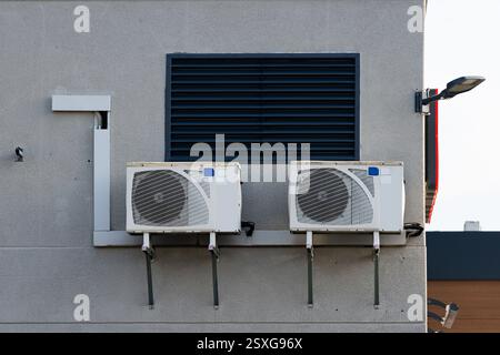 Zwei weiße Klimaanlagen sind sicher an der Außenwand eines Geschäftsgebäudes montiert und sorgen für Luftzirkulation und Kühlung im Innenraum. Stockfoto
