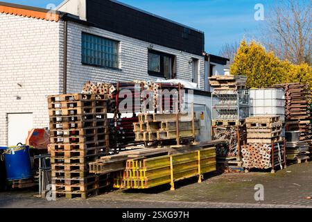 In einem Lagerbereich befinden sich Stapel von Holzpaletten und Baugerüste. Helles Sonnenlicht unterstreicht die geordnete Anordnung. Der Hintergrund umfasst Stockfoto