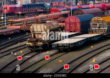Auf einem belebten Bahnhofsgelände stehen verschiedene Güterwagen, die auf mehreren Gleisen unter klarem blauem Himmel geparkt sind. Leuchtend rote Markierungen und ein gut organisiertes Layout Stockfoto