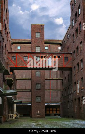 Innenhof eines Industriebaus in Deutschland mit roter Skybridge und verwitterter Ziegelfassade. Stockfoto