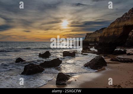 Morgenstrand bei Sonnenaufgang und Felsen im Vordergrund am Strand Praia da Batata in Lagos Portugal mit goldenem Himmel Stockfoto