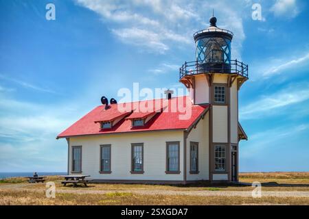 Ein bezaubernder Leuchtturm, bekannt als Point Cabrillo, mit einem hellroten Dach, steht auf einer grasbewachsenen Landschaft unter einem klaren blauen Himmel. Seine weiße Fassade und Umgebung Stockfoto