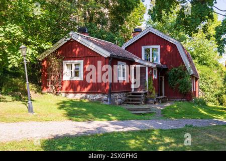 Allgemeiner Blick auf ein typisch schwedisches Falu-Rotes Blockhaus mit einem Gambrel-Dach im Wald an einem sonnigen Sommertag. Stockfoto