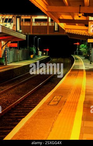 Hier ist eine Bildunterschrift: Eine ruhige Nacht am Bahnhof. Die Bahnsteige sind leer und werden durch das warme Leuchten der Bahnhofslichter beleuchtet. Stockfoto