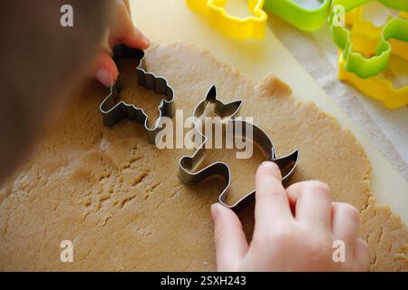 Junge Hände schneiden verschiedene Formen aus gerolltem Lebkuchenteig mit Osterschneidern. Der Prozess der Osterkekse. Stockfoto