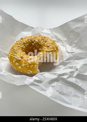 Gebissener gelber Donut in weißem Papier auf weißem Tisch Stockfoto