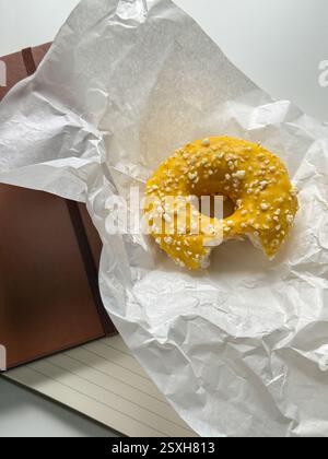 Gebissener gelber Donut in weißem Papier auf dem Bürotisch Stockfoto