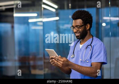 Junger, erfolgreicher erfahrener Arzt, der mit einem Tablet-Computer in der Hand in der Klinik steht. Der Arzt überprüft die Patientendaten und kommuniziert mit den Kunden aus der Ferne. Stockfoto