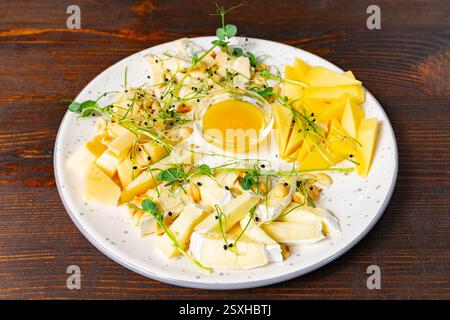 Auf der wunderschön angeordneten Käseplatte finden Sie verschiedene Käsesorten, Honigdip und frische Beilagen. Die Präsentation hebt Texturen und Farben hervor. O Stockfoto