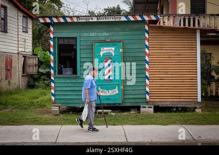 Ein älterer Mann mit einem Gehstock geht an Dougy's Barbershop in San Ignacio, Cayo District, Belize vorbei. Stockfoto