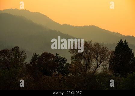 Mehrschichtige Bergsilhouetten und Bäume bei Sonnenuntergang Stockfoto
