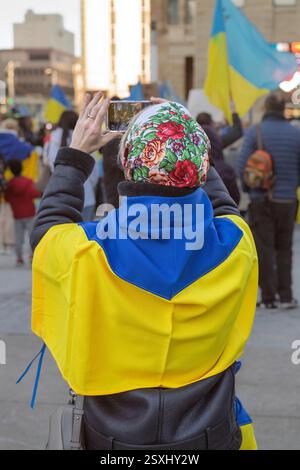 Eine Person, die eine ukrainische Flagge trägt, macht ein Foto während einer öffentlichen Demonstration mit Fahnen und Bannern in Calgary, Alberta. Februar 2025 Stockfoto