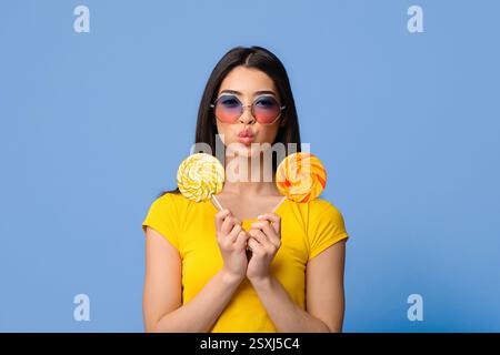 Verspielte Asiatische Frau In Stilvollen Sonnenbrille Posiert Mit Zwei Lollipop In Händen Stockfoto