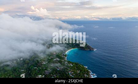 Wolken ziehen über die Bucht, wenn die Sonne aufgeht, mit türkisfarbenem Wasser und einer üppig grünen Küste. Seychellen, Mahe. Stockfoto