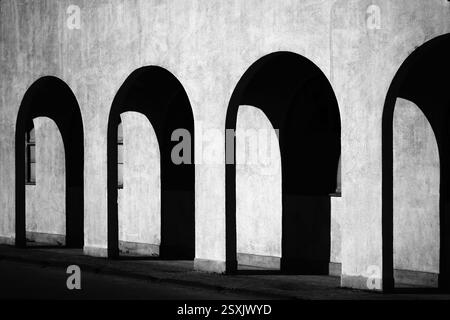 Schwarzweiß-Schwarzweiß-Liminal Space schöne Architekturfotografie, die sich wiederholende Muster von Licht und Schatten durch den gewölbten Außenflur des zeigt Stockfoto
