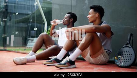 Tennis, Sport oder Männer mit Pause auf dem Platz zum Ausruhen, Trinken von Wasser oder Match-Training Ermüdung. Padel, Freunde oder entspanne dich beim Fitnesstraining für Stockfoto