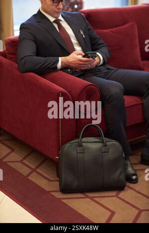 Geschäftsmann sitzt auf der Couch und hält Smartphone Stockfoto