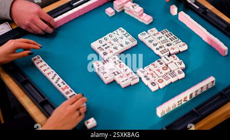 Ein Mahjong-Tisch mit einem aktiven Spiel und den Händen eines Spielteilnehmers. Ein altes asiatisches Spiel namens Mahjong, um sich zu entspannen und Spaß zu haben. F Stockfoto