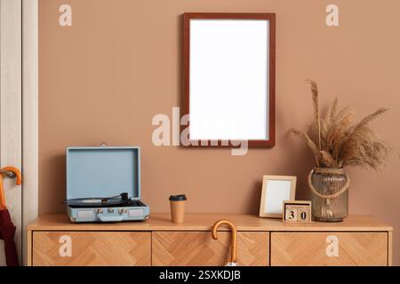 Holzschrank mit Plattenspieler, Pampas-Gras in Vase und leerer Rahmen im modernen Flur Stockfoto