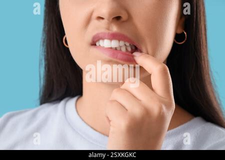 Junge Frau, die ihre Zähne auf blauem Hintergrund zeigt, Nahaufnahme Stockfoto