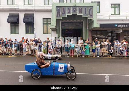 Seifenboxen-Derby-Rennen in den Straßen von Napier, Neuseeland, während des Art déco-Festivals. Kinder radeln am historischen Masonic Hotel vorbei Stockfoto
