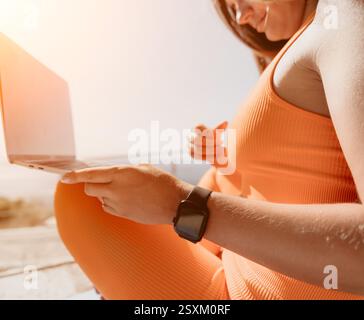 Frau in Orange Workout Kleidung benutzt einen Laptop und eine Smartwatch Stockfoto