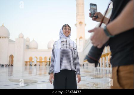 Ein Fotograf fotografiert eine Frau in einem Kopftuch mit ihrem Handy in der Scheich-Zayed-Moschee. Freunde, die Abu Dhabi besuchen und M Stockfoto