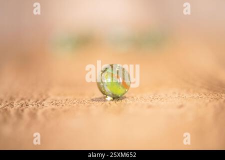 Ein einzelnes Glas marmoriert auf einer Holzoberfläche mit komplizierten Drallmustern und reflektierendem Licht, nostalgisch und verspielt Stockfoto