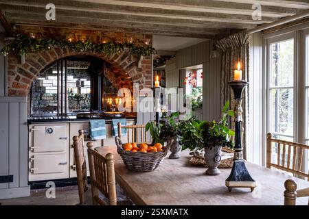 Spiegelfliesen hinter gusseisernem Esse-Herd, der Kerzenlicht reflektiert, im renovierten Bauernhaus East Sussex Tudor aus dem Jahr 1540 in England, Großbritannien. Stockfoto