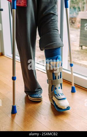 Detail einer gebrochenen Bein- oder Fußverletzung beim Gehen auf Krücken mit Beinstütze, Anbringen einer Orthese oder Bandage zur Stützung des Sprunggelenks nach Beinoperationen Stockfoto