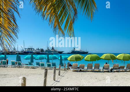 Stühle und Sonnenschirme am Great Bay Beach mit Booten im Yachthafen von Philipsburg, karibische Landschaft, Insel St. Maarten (St. Martin), niederländische Westindien Stockfoto