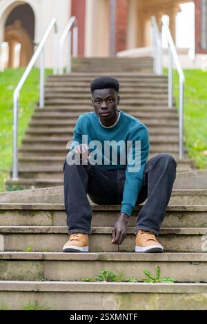 Porträt eines selbstbewussten afroamerikanischen Studenten, der auf der Treppe eines Universitätsgeländes sitzt Stockfoto