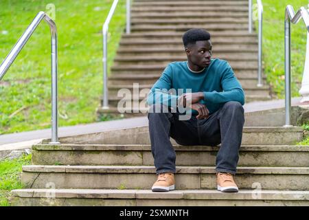 Nachdenklicher junger Mann, der auf Stufen in einem Park sitzt, schaut weg Stockfoto