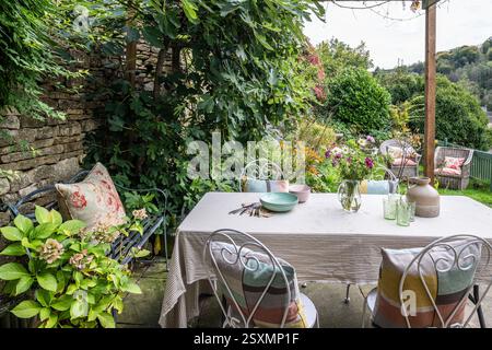 Tisch und Stühle schattiert von Feigenbaum auf der Terrasse des Chalford Weavers Cottage in den Cotswolds, Gloucestershire, England, Großbritannien. Stockfoto