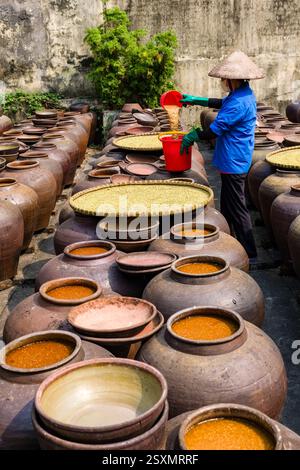 Sojasauce wird in großen Töpfen aus Steingut in einem Hinterhof im kleinen Dorf Bần Yên Nhân am Stadtrand von Hanoi hergestellt, zwei Frauen mit konischen Hüten Stockfoto