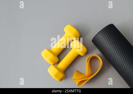 Zwei Kurzhanteln, Yogamatte, Fitnessband und Thermosflasche auf grauem Hintergrund, flache Lay. Stockfoto