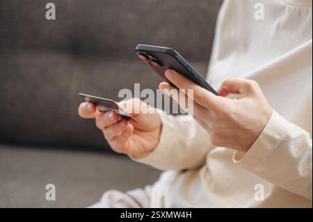 Das Mädchen bezahlt für Einkäufe mit dem Smartphone, das eine Bankkarte in der Hand hält. Hochwertige Fotos Stockfoto