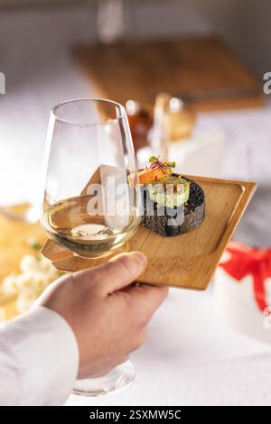 Nahaufnahme eines Kellners, der ein Glas Weißwein und schwarze Brotkanapees auf einem kleinen Holztablett serviert Stockfoto