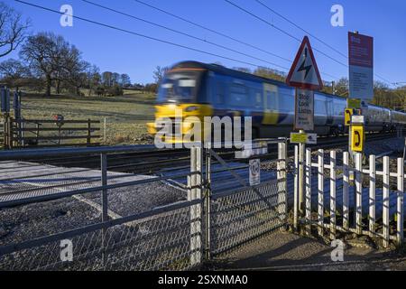 Northern Rail Zug fährt über unbemannte Bahnübergänge (streckenseitige Eisenbahnwarnungen) - Burley in Wharfedale, West Yorkshire, England, Großbritannien. Stockfoto