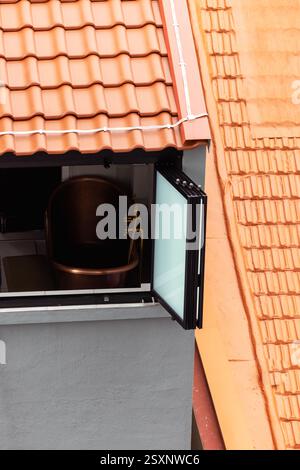 In der Mitte des orange gekachelten Dachs befindet sich ein offenes Fenster aus modernen Materialien. Stockfoto