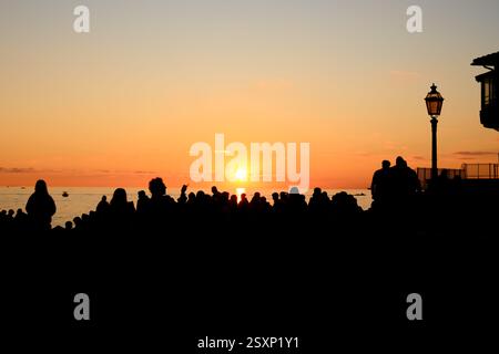 Rückansicht einer Menschenmenge Silhouetten, die den Sonnenuntergang draußen am Strand im alten Fischerdorf Boccadasse, Genua, Ligurien, Italien genießen Stockfoto