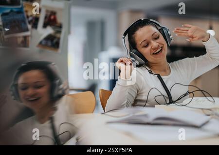 Fröhlicher Schüler, der Musik hört, während er zu Hause studiert Stockfoto