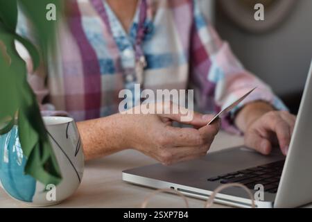 Frau, die am Schreibtisch vor dem Laptop sitzt und eine Kreditkarte hält Stockfoto