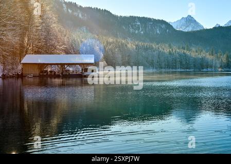 Dieses Foto zeigt eine ruhige Winterszene an einem ruhigen See. Das Bild zeigt ein hölzernes Dock, das in das Wasser hineinreicht und teilweise mit einem s bedeckt ist Stockfoto